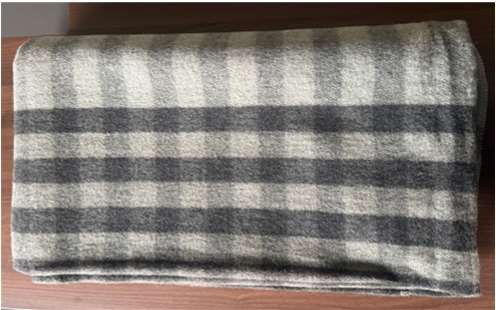 Close view of the texture and stitched edge of a grey checked pure wool blanket